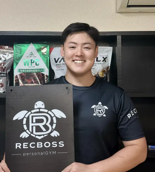 Recbossのロゴボードを持って笑顔で立つ代表トレーナー 川隅蒼生（Aoi）